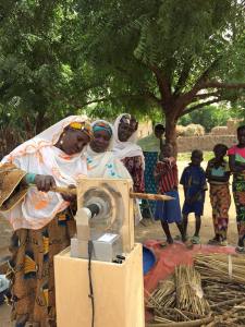 A woman threshes a panicle using the HIT AF2 prototype while a line forms behind her and children look on.