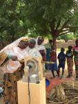 A woman threshes a panicle using the HIT AF2 prototype while a line forms behind her and children look on.